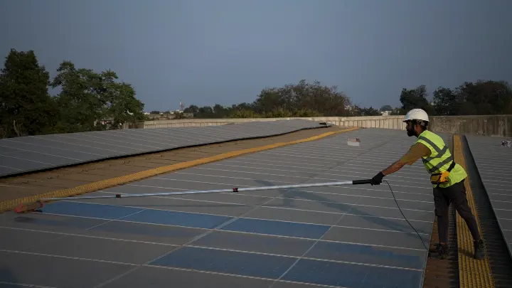 Technician cleaning a large rooftop solar array with a long-reach waterless cleaner